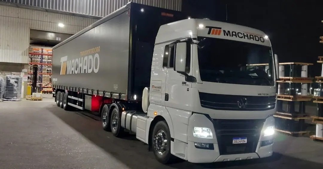Caminhão da Transportadora Machado na doca de armazenamento com estantes de paletes ao fundo